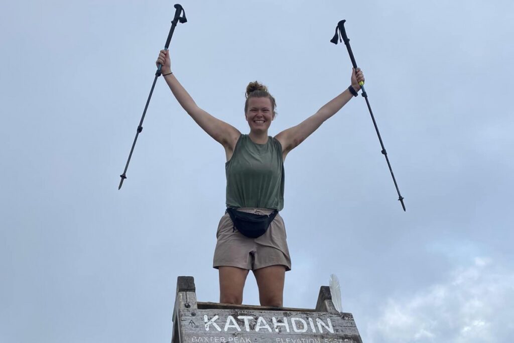 Lyndsay Monsen holding up her walking sticks at the top of a summit
