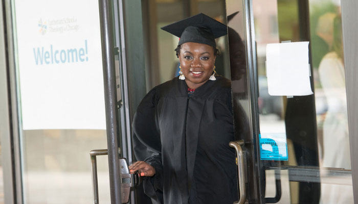 An LSTC graduate coming through the door of the LSTC entrance in their cap and gown