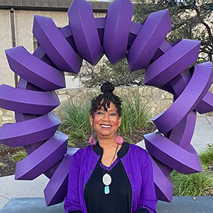 Dr. Linda Thomas poses in front of the purple “The Geometry of Space and Time” sculpture in San Antonio in a matching outfit.