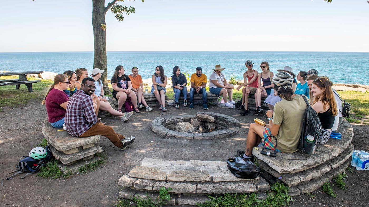 A group of students chat around a fire pit at Promontory Point in Hyde Park, Chicago