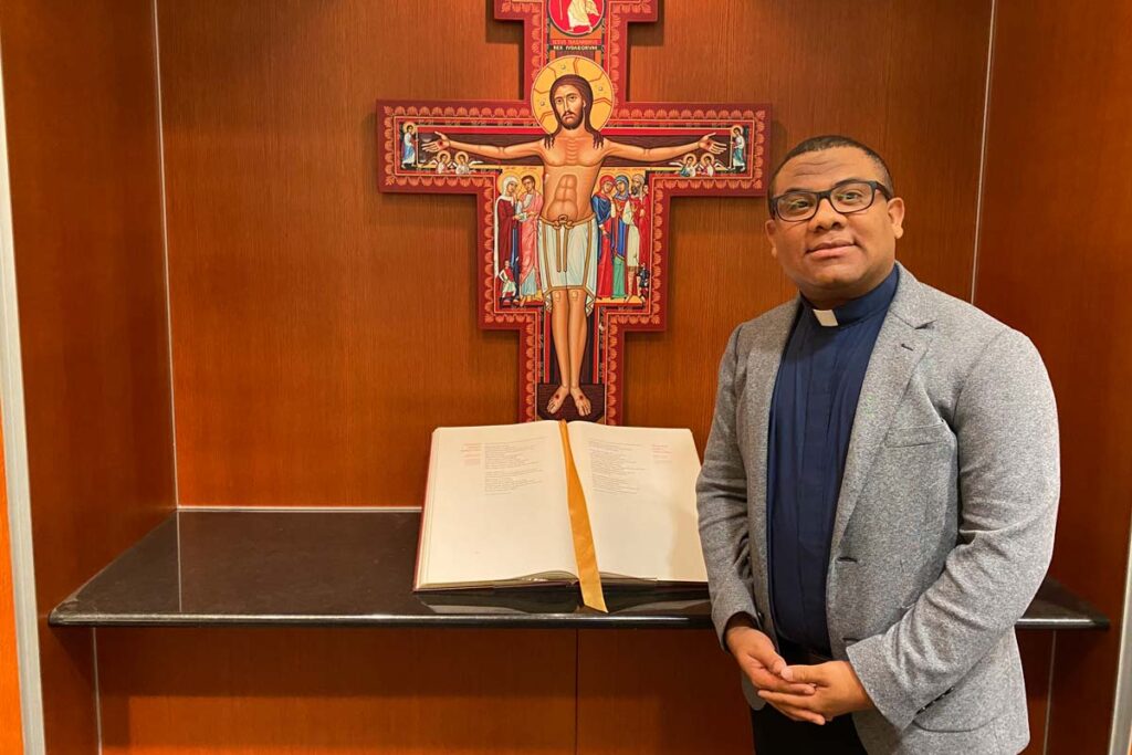 Juan Manuel Perea poses in front of a painted crucifix and book