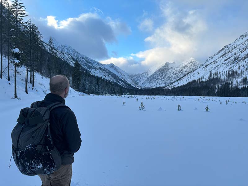 A man in a backpack looks out toward the Cascade Mountains