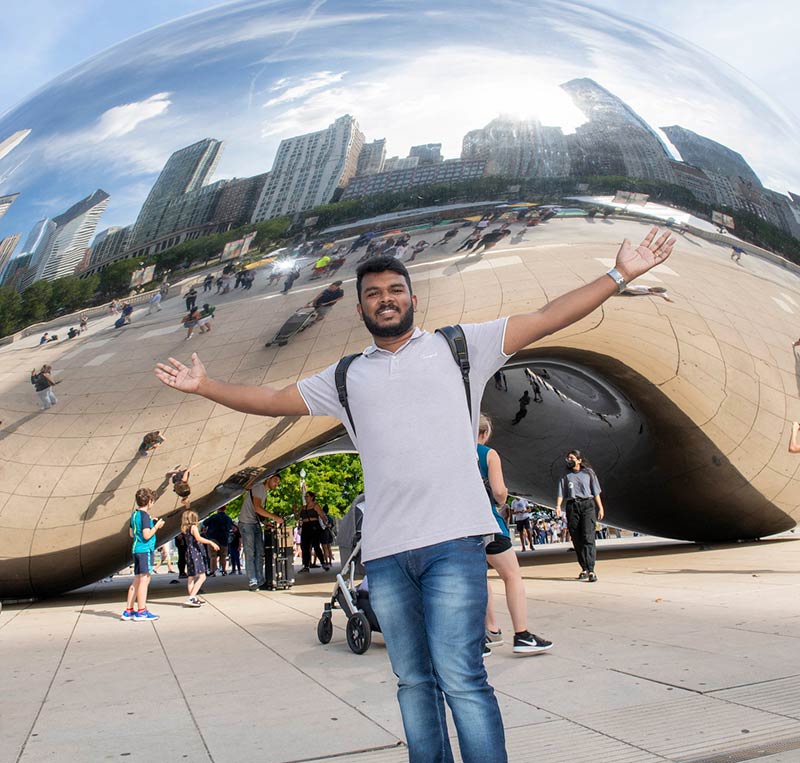 An incoming LSTC student posing with his arms up in front of The Bean in downtown Chicago.