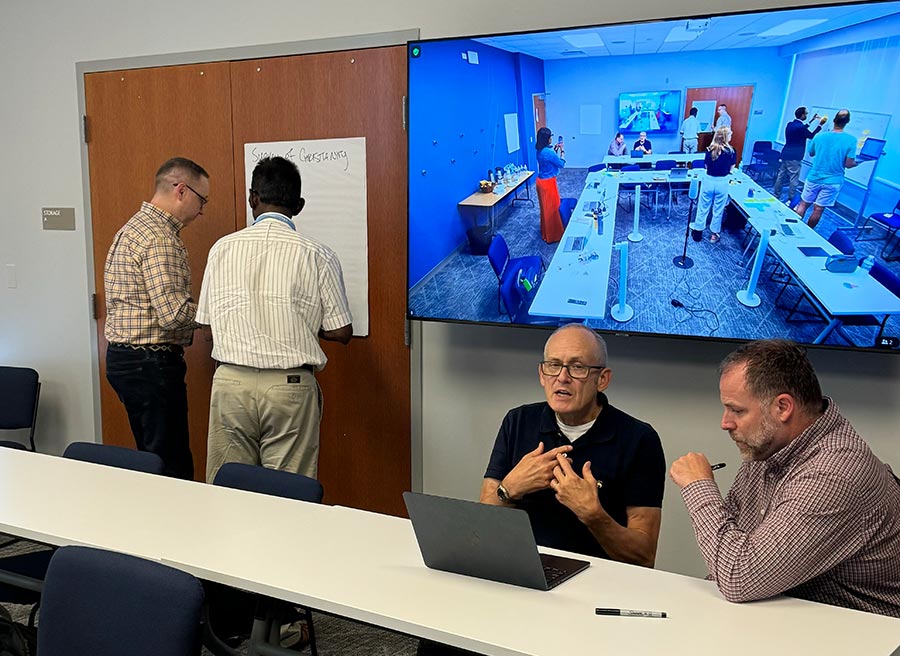 LSTC Faculty and Noodle representatives brainstorming: two men are sitting around a computer while another two men are writing ideas down on a large workboard.