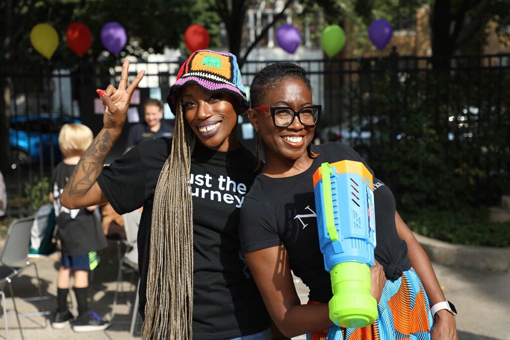 Two women posing: one with a peace sign and the other holding a super soaker.