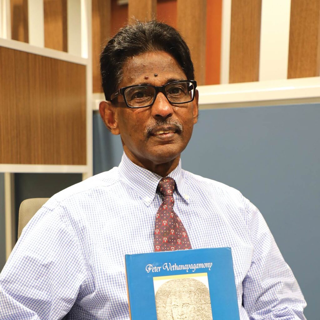 Professor Peter Vethanayagamony holding up a copy of his book.