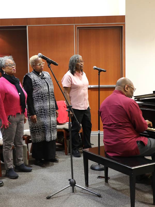 Conductor Dr. Keith Hampton playing piano with a line of singers behind him during rehersal.
