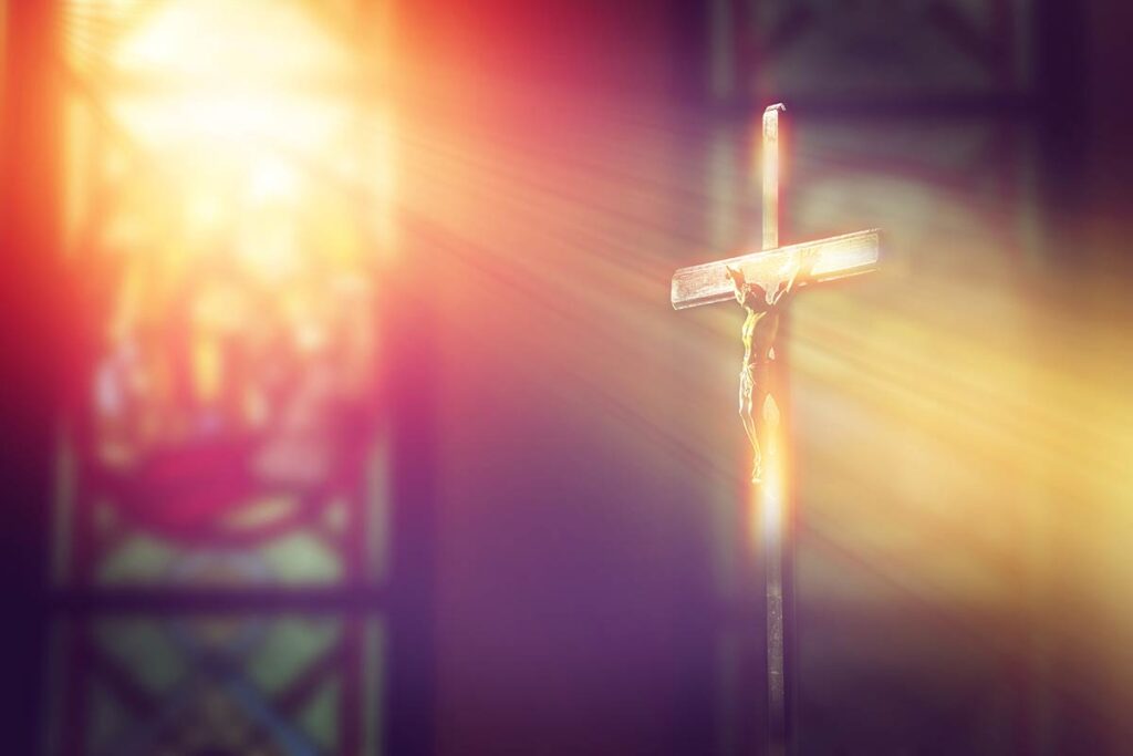 Light pouring through stained glass illuminating a crucifixion.