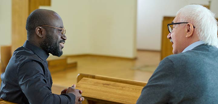 A pastor and parishioner conversing in the pews.