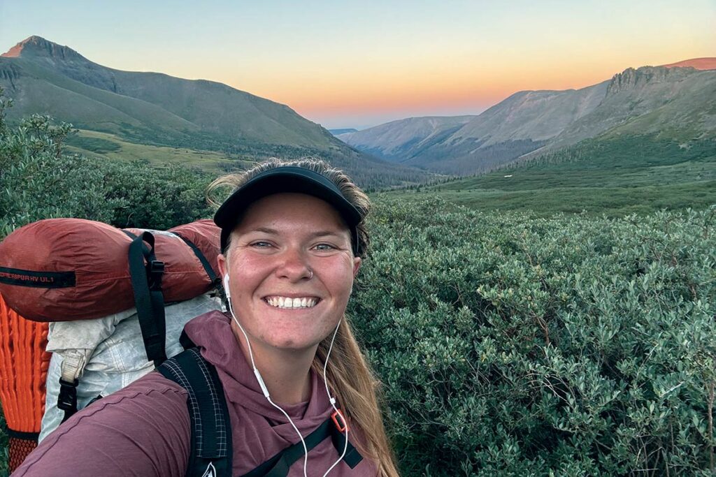 Lyndsay Monsen backpacking with beautiful mountains and the sunset behind her.