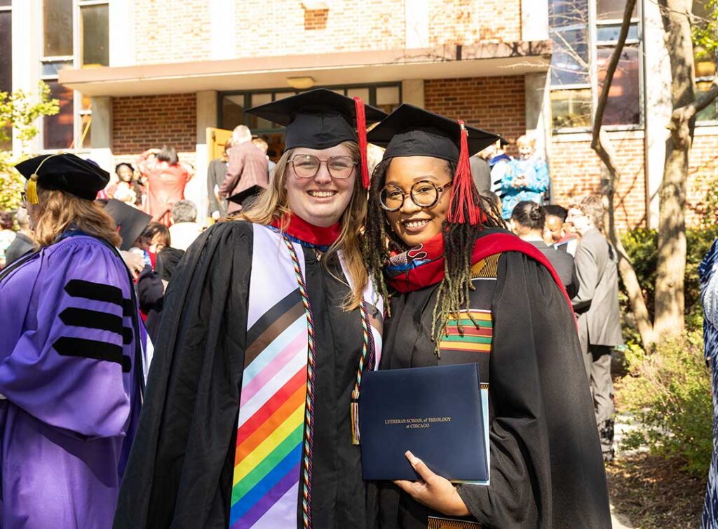 Two smiling LSTC grads, one wearing rainbow stoles.