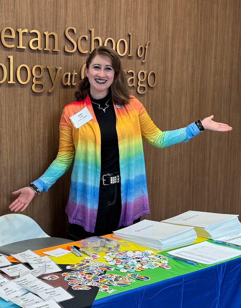 Alex welcoming attendees to the Queer Symposium with a selection of swag.